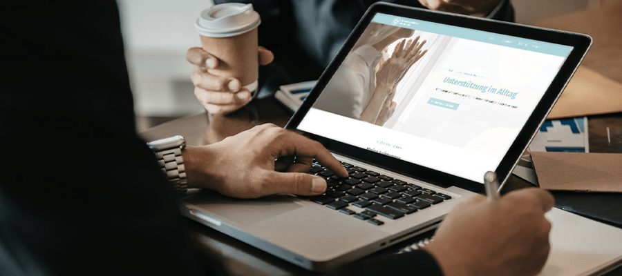 Website eines Betreuungsdienstes mit Händen älterer Personen auf einem Laptop-Display