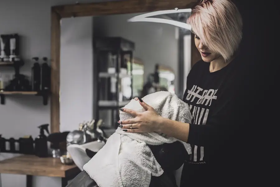 Website für Friseure - Friseurin im modernen Salon wickelt einem Kunden ein Handtuch um den Kopf – professionelle Haarpflege und Wohlfühlatmosphäre.